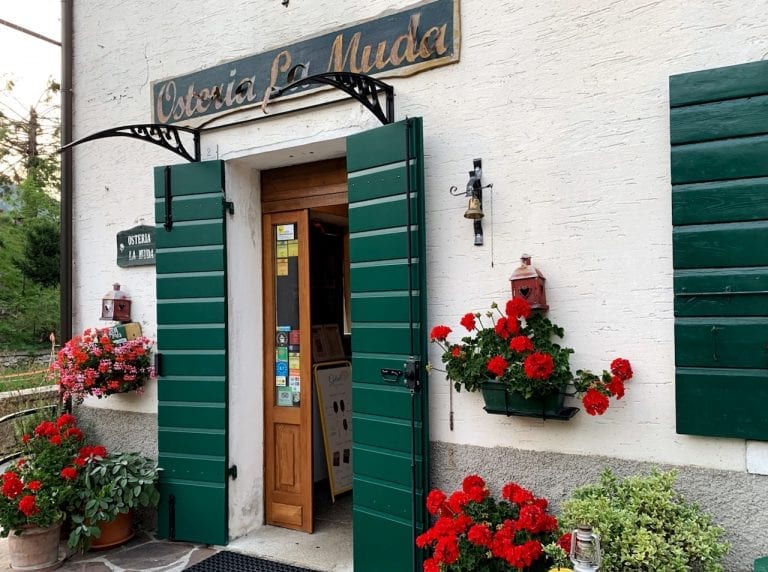 the entrance of osteria la muda is like a farmhouse with flowers and very clean colors